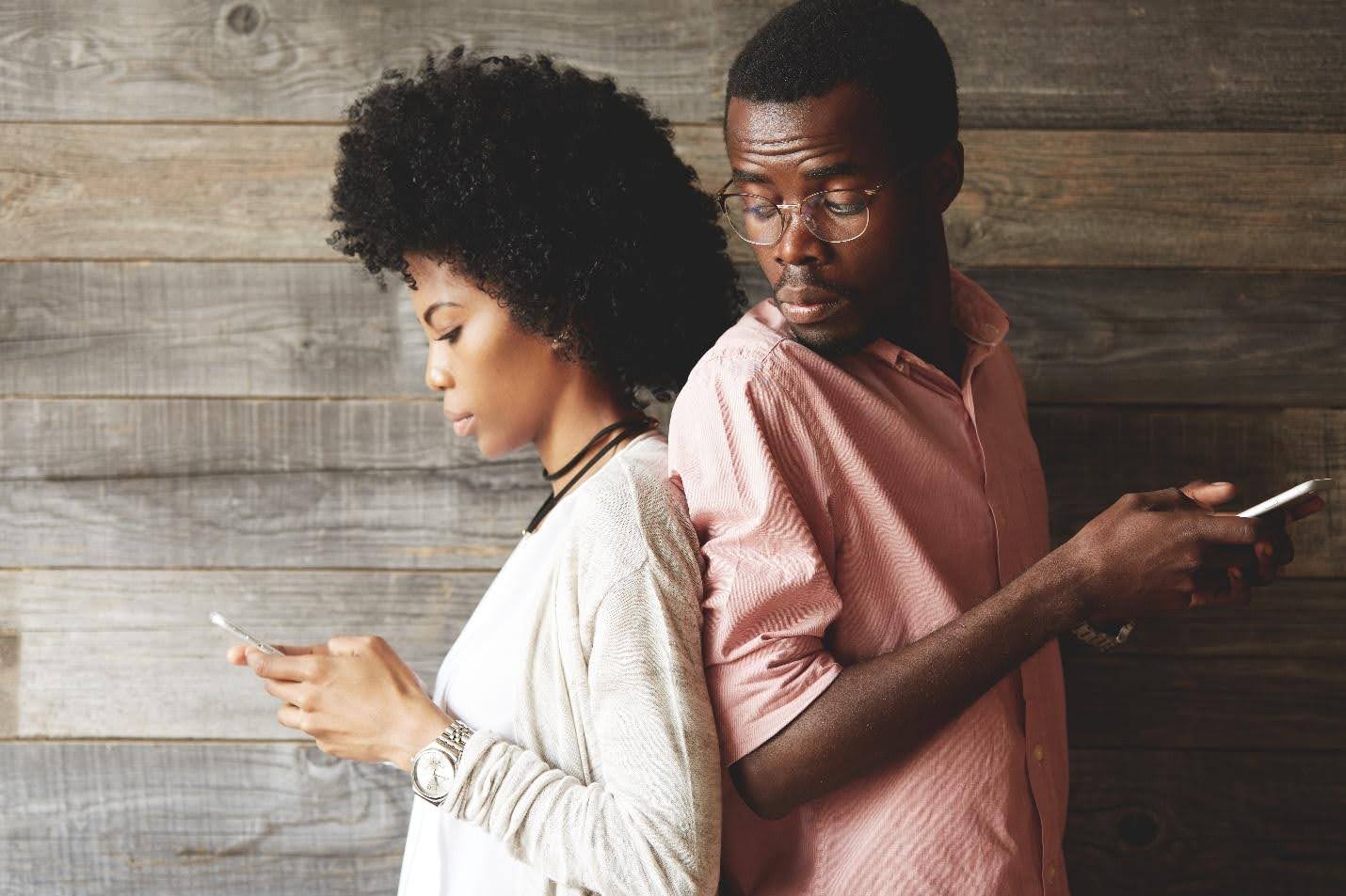 couple texting while standing back-to-back